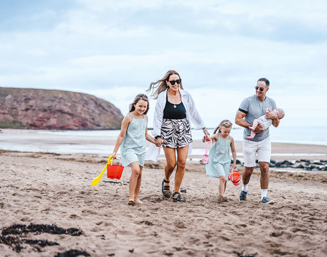 Family walking along the beach at Pease Bay with buckets and spades 
