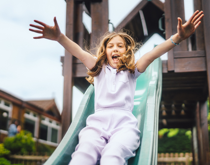 Young girl smiling and playing on a slide in a playground 