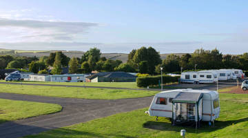 A high angle image of touring vans and motorhomes parked on touring pitches in a grassy field at a holiday park on a sunny day 