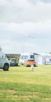 Two touring vans and cars parked on touring pitches at a UK holiday park with green grass and a blue sky above 