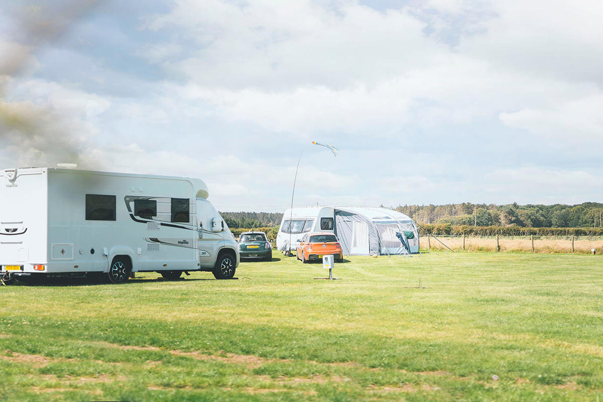 Two touring vans and cars parked on touring pitches at a UK holiday park with green grass and a blue sky above 