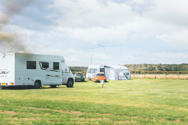 Two touring vans and cars parked on touring pitches at a UK holiday park with green grass and a blue sky above 
